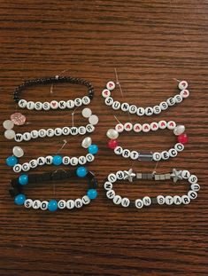 several bracelets with letters and beads on them sitting on a wooden table next to each other