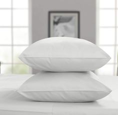 three white pillows stacked on top of each other in front of a table with two vases