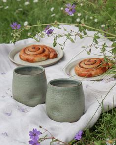 two small cups sitting on top of a white towel next to pastries and flowers