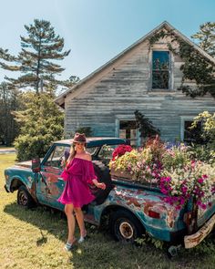 a woman in a pink dress standing next to an old truck with flowers on the bed