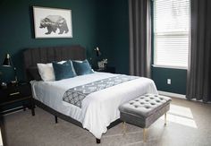 a bedroom with green walls and white bedding in the corner, along with a gray footstool