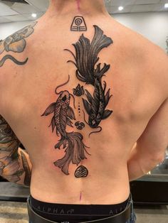 the back of a man's tattoo with fish and flowers on his upper back