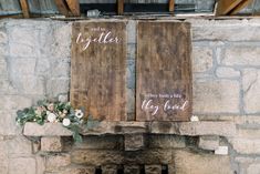 two wooden signs hanging from the side of a stone wall next to a fire place