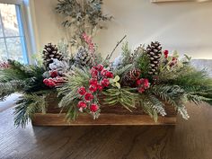 a wooden box filled with pine cones and red berries sitting on top of a table