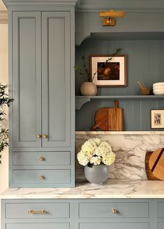 a kitchen with blue cabinets and marble counter tops, white flowers in a vase on the island