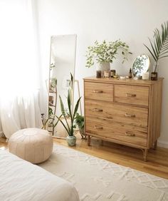 a bedroom with a bed, mirror and plants on the dresser next to each other