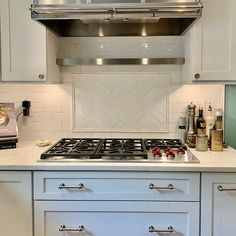 a stove top oven sitting inside of a kitchen next to white cupboards and drawers