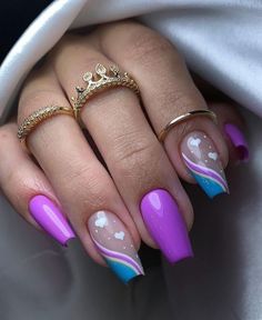 a woman's hand with purple and blue nail polishes on her nails, holding a gold ring