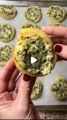 a person holding up a pastry with spinach on it in front of some muffins