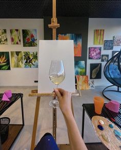 a person holding a wine glass in front of an easel