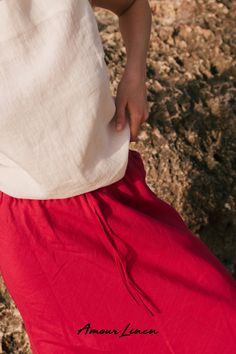 a woman in a white top and red skirt is walking on the rocks with her hand over her hip