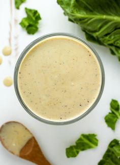 a glass filled with dressing sitting on top of a table next to lettuce