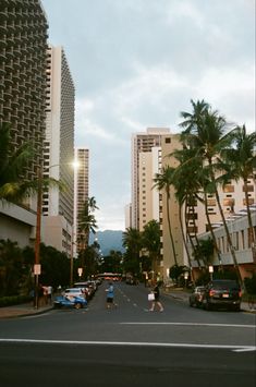 people are walking down the street in front of tall buildings with palm trees on both sides