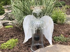 an angel - shaped glass bottle is sitting on the ground in front of some plants