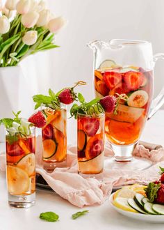 two pitchers filled with fruit and ice on top of a white table next to bowls of berries