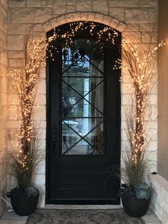 the front door is decorated with christmas lights and potted plants, along with two large black planters