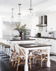 a kitchen with white cabinets and wooden chairs around a table in front of an island