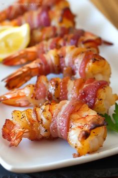 shrimp and bacon skewers on a white plate with lemon wedges