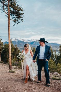 a bride and groom walking down a trail in the mountains