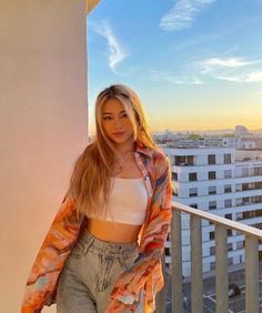 a beautiful young woman standing on top of a balcony next to a tall white building