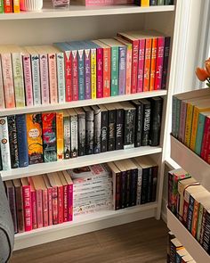 a book shelf filled with lots of books next to a chair and vase full of flowers