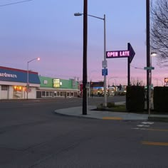 an open late sign on the corner of a city street at dusk with buildings in the background