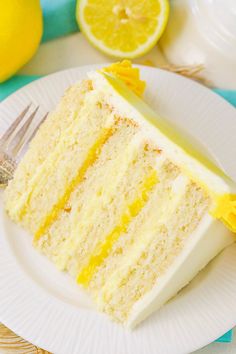 a slice of lemon cake on a white plate with a fork and some lemons in the background