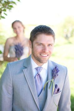 a man in a gray suit and tie with a flower on his lapel is smiling at the camera