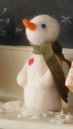 a white snowman with a scarf around his neck and book in front of him