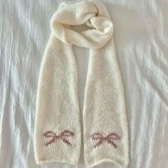 a white scarf with red stitches on it laying on top of a bed next to a pillow