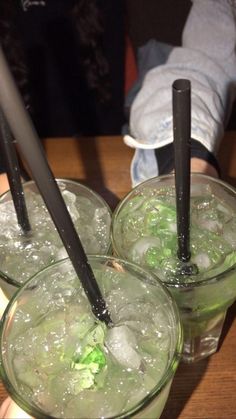 three glasses filled with ice sitting on top of a wooden table next to a person