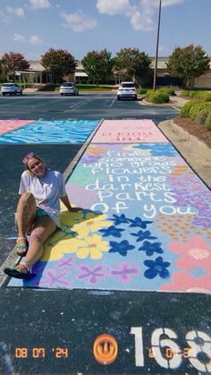 a woman sitting on the ground in front of a parking lot with colorful chalk drawings