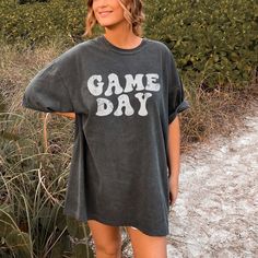 a woman wearing a black tshirt stands in front of some bushes and grass