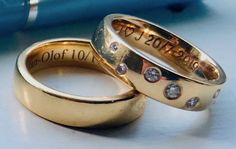 two gold wedding rings with diamonds on them sitting next to a blue pen and book