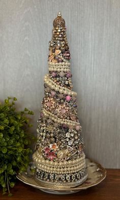 a christmas tree made out of buttons and pearls on a silver platter next to a potted plant