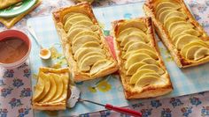 there are four slices of bread with apples on the table next to some dipping sauces