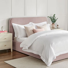 a bed with white sheets and pink pillows