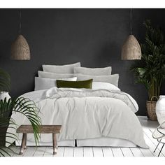 a bed with white linens and pillows in a room decorated with potted plants