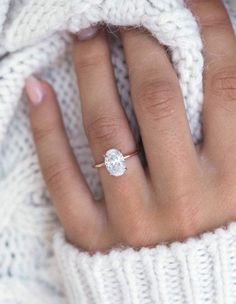 a woman's hand with a diamond ring on top of her finger, in front of a white sweater