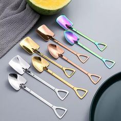 six spoons with different shapes and colors on top of a gray table next to a watermelon