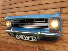 an old blue car parked on the side of a wooden building next to a wall