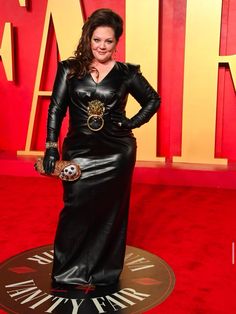 a woman in a black dress standing on a red carpet with her hands on her hips