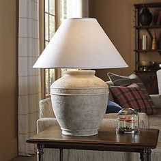 a table with a lamp on top of it in front of a couch and window