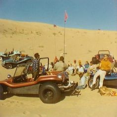 several people sitting in the sand next to cars and jeeps with flags on them