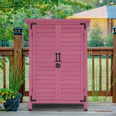 a pink storage shed sitting on top of a wooden deck next to a planter