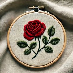 a close up of a red rose embroidered on a white piece of cloth with green leaves