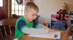 a young boy sitting at a table with a pen and paper