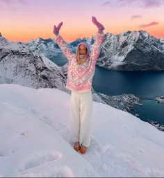 a woman standing on top of a snow covered mountain with her arms in the air