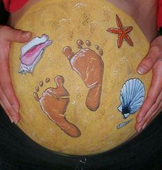 a pregnant woman holding a yellow plate with pictures of baby feet and seashells on it