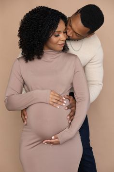 a pregnant woman hugging her husband's belly in front of a beige background for an image